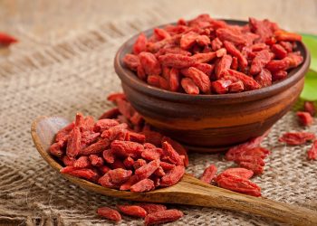 Bowl and spoon filled with dried goji berries on burlap.