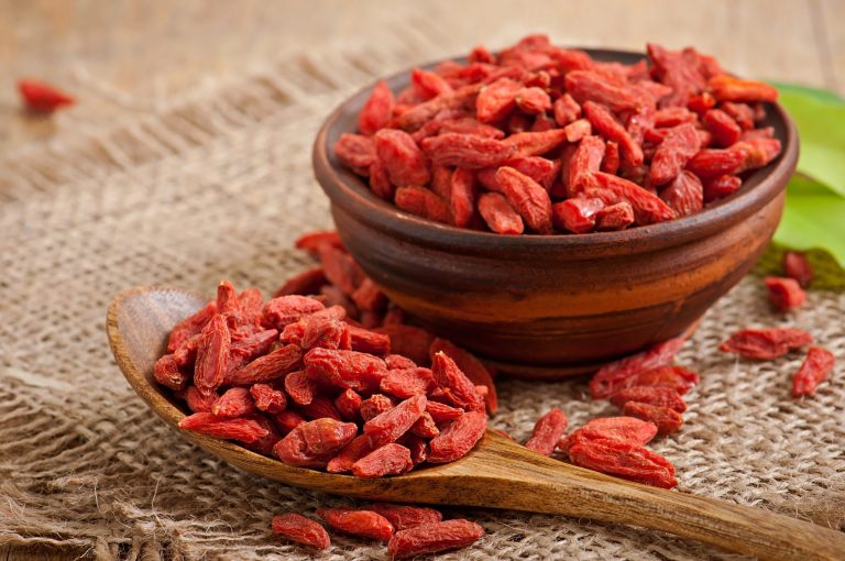 Bowl and spoon filled with dried goji berries on burlap.