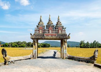 Ornate entrance with stone carvings leading to rice fields.