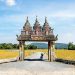Ornate entrance with stone carvings leading to rice fields.