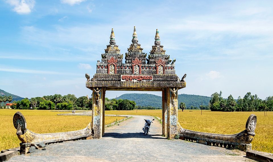 Ornate entrance with stone carvings leading to rice fields.