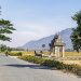 Rural road leading to traditional Cambodian gate, with distant mountains.