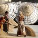 Women sorting grain at a mill with large storage baskets in the background.