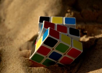 Rubik's Cube partially buried in sand on a sunny day.
