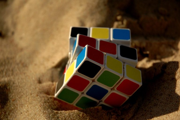 Rubik's Cube partially buried in sand on a sunny day.