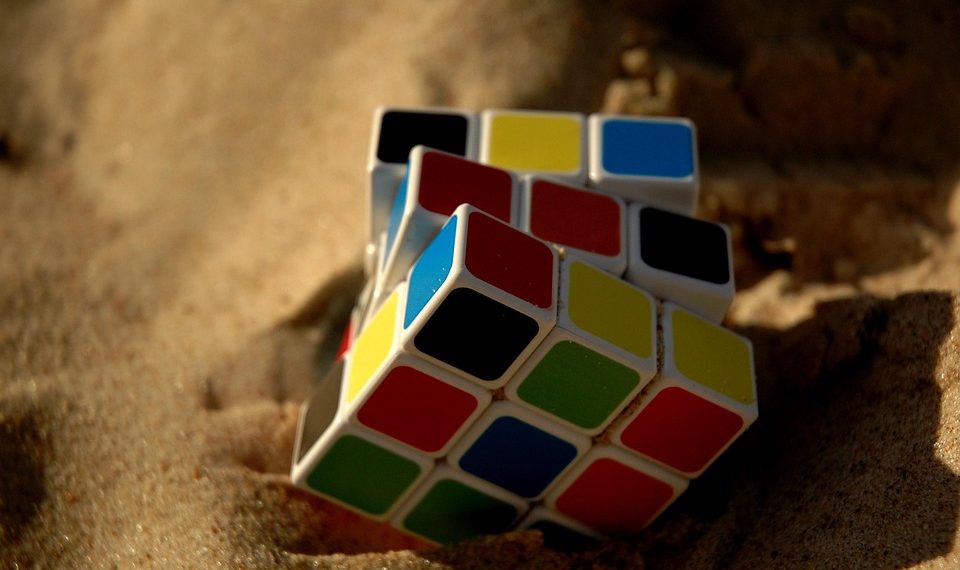 Rubik's Cube partially buried in sand on a sunny day.
