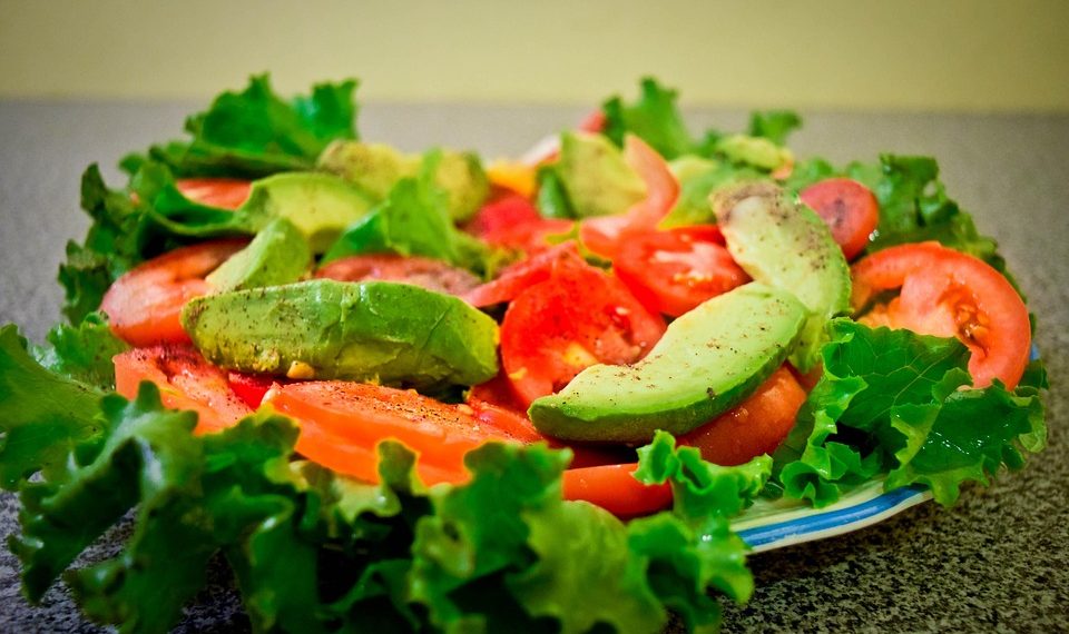 Fresh salad with lettuce, tomato, and avocado slices on a plate.