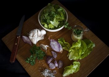 Fresh lettuce, garlic, and herbs on a wooden cutting board.