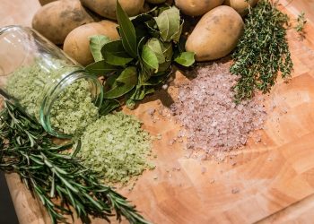 Herbs, spices, and potatoes on a wooden board.