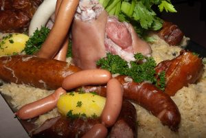 Boiled pork knuckle with assorted sausages, sauerkraut, and potatoes garnished with parsley.