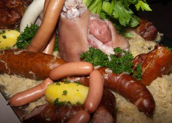 Boiled pork knuckle with assorted sausages, sauerkraut, and potatoes garnished with parsley.