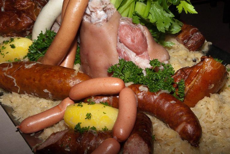 Boiled pork knuckle with assorted sausages, sauerkraut, and potatoes garnished with parsley.