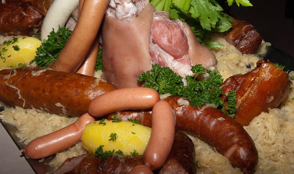 Boiled pork knuckle with assorted sausages, sauerkraut, and potatoes garnished with parsley.
