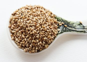 Spoon filled with sesame seeds on a decorative ceramic scoop.
