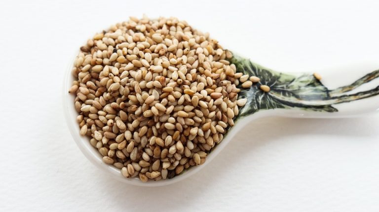Spoon filled with sesame seeds on a decorative ceramic scoop.