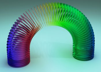 Colorful rainbow Slinky toy arched gracefully on a light blue background.