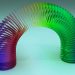Colorful rainbow Slinky toy arched gracefully on a light blue background.