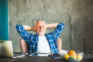 Man relaxing at desk with laptop, wearing blue plaid shirt.