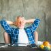Man relaxing at desk with laptop, wearing blue plaid shirt.