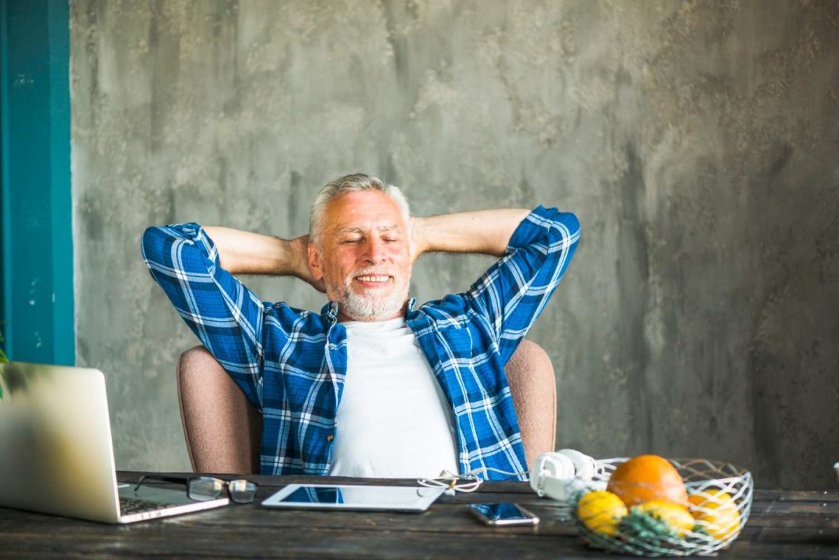 Man relaxing at desk with laptop, wearing blue plaid shirt.