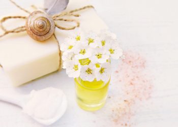 White flowers in a small jar beside natural soap and a feather.