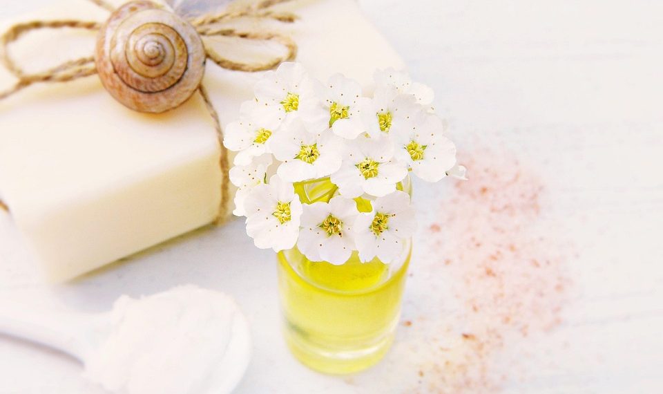 White flowers in a small jar beside natural soap and a feather.