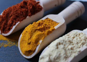 Colorful spices in wooden scoops on a dark surface.