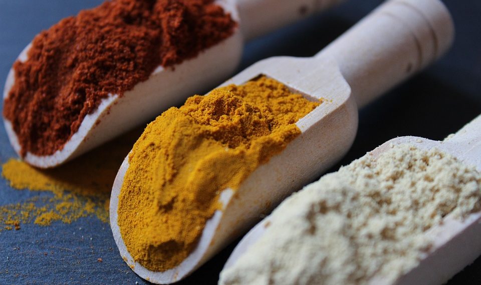 Colorful spices in wooden scoops on a dark surface.