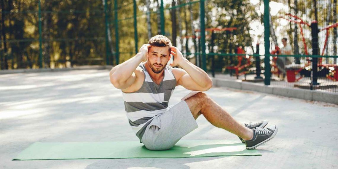Man doing sit-ups on a green mat outdoors, focusing on exercise.