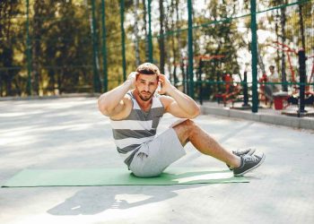 Man doing sit-ups on a green mat outdoors, focusing on exercise.