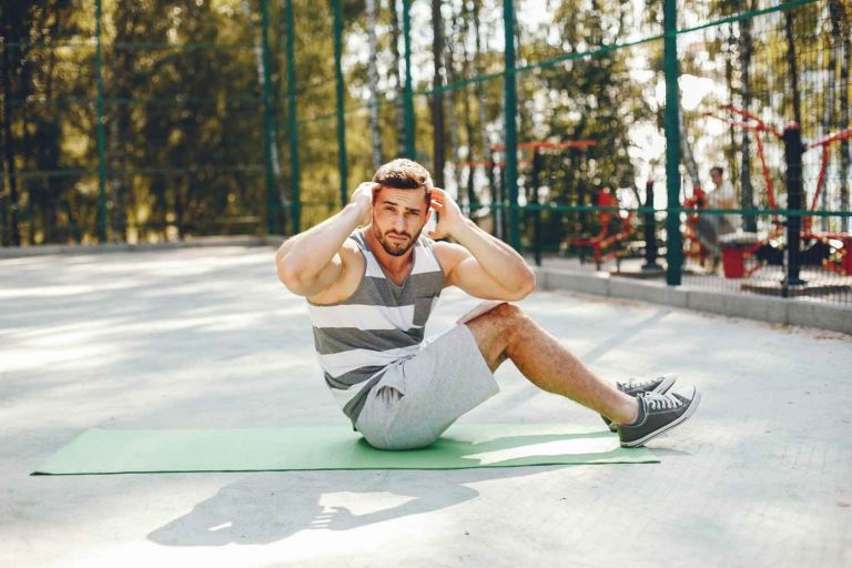 Man doing sit-ups on a green mat outdoors, focusing on exercise.