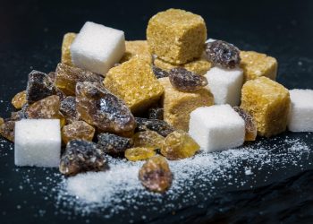 A mix of brown and white sugar cubes alongside raw amber and dark sugar crystals on a dark surface.