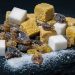 A mix of brown and white sugar cubes alongside raw amber and dark sugar crystals on a dark surface.