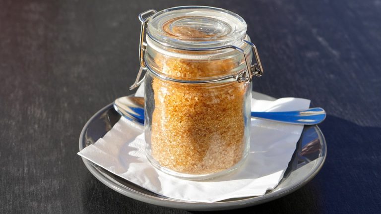 Jar of brown sugar on a plate with spoon.