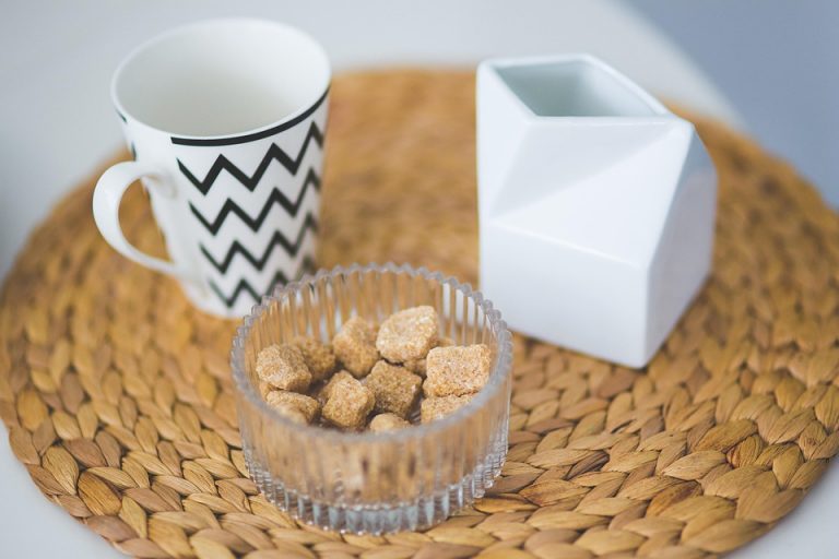 Chevron mug with sugar cubes in bowl on woven placemat.