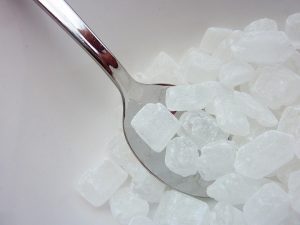 Silver spoon scooping crystal sugar cubes from a bowl.