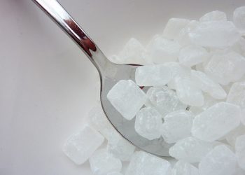 Silver spoon scooping crystal sugar cubes from a bowl.