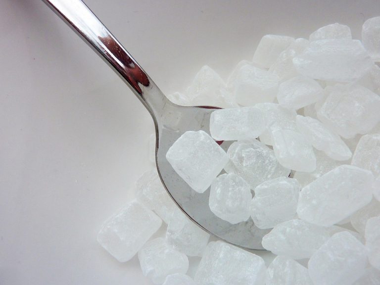 Silver spoon scooping crystal sugar cubes from a bowl.