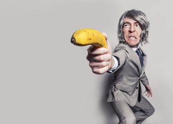 Man in suit humorously aiming a banana as a weapon.