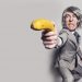 Man in suit humorously aiming a banana as a weapon.