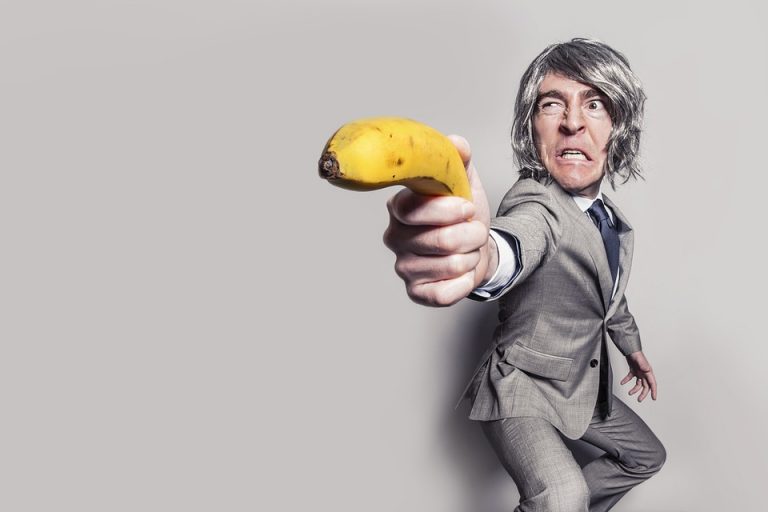 Man in suit humorously aiming a banana as a weapon.