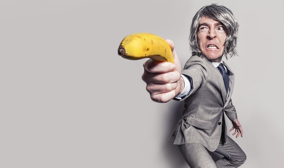 Man in suit humorously aiming a banana as a weapon.