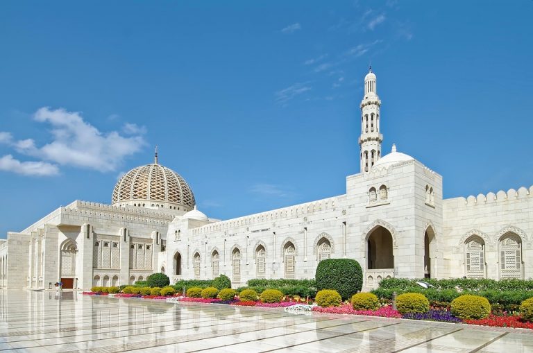 Grand mosque exterior with gardens under blue sky.