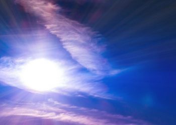 Bright sun radiating through wispy clouds in a clear blue sky.