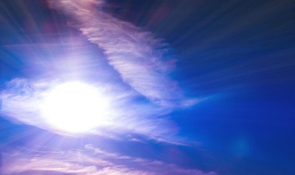 Bright sun radiating through wispy clouds in a clear blue sky.