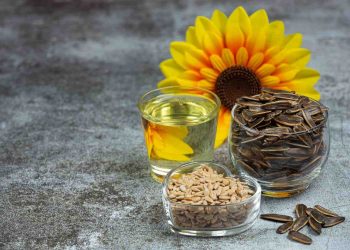 Sunflower seeds, oil, and flower displayed on a table.
