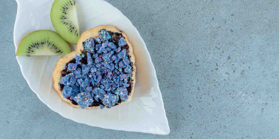 Heart-shaped pastry with blue topping and kiwi slices on leaf plate.