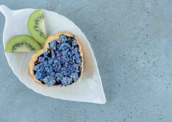 Heart-shaped pastry with blue topping and kiwi slices on leaf plate.