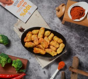 Golden fried snacks on a black platter surrounded by fresh spices and vegetables.