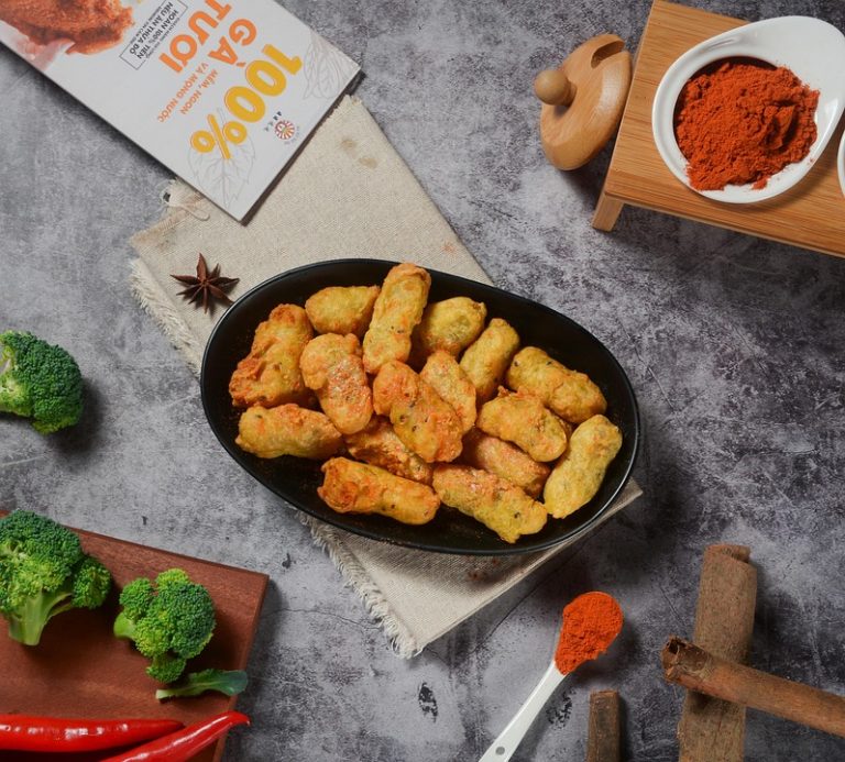 Golden fried snacks on a black platter surrounded by fresh spices and vegetables.